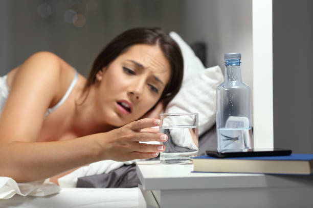 Dehydrated woman reaching a glass of water on the bed in the night at home